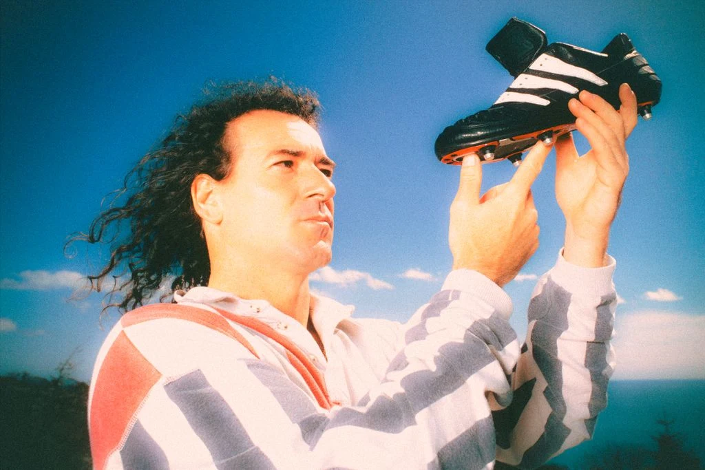 Craig Johnston holding up an original adidas Predator boot against a blue sky
